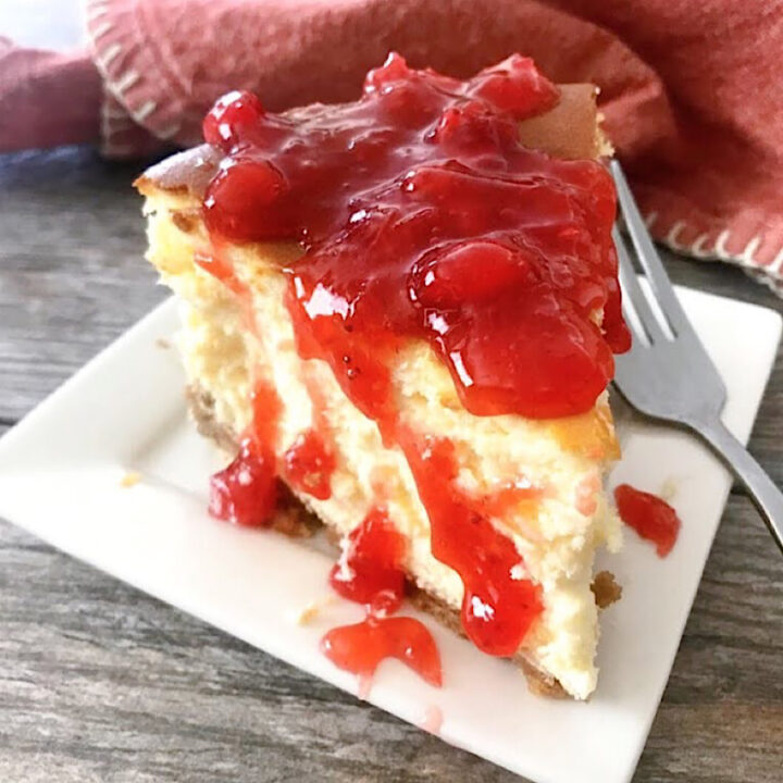 A slice of New York style cheesecake topped with strawberry sauce.