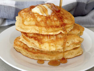 A stack of sweet cream pancakes on a plate topped with butter and syrup.