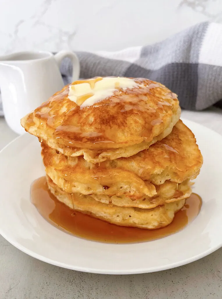A stack of sweet cream pancakes on a plate topped with butter and syrup.