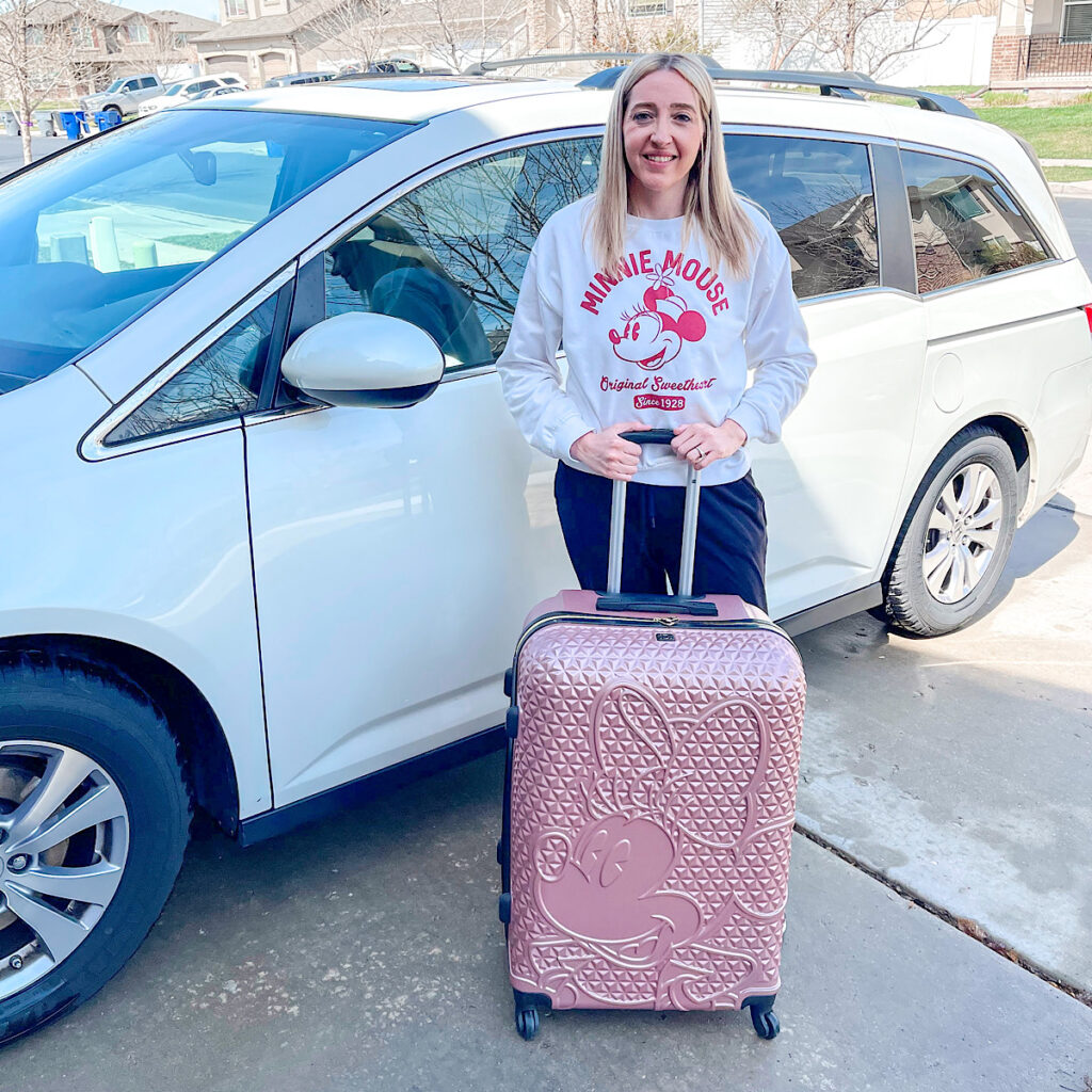 Someone standing by a white minivan with a pink Minnie Mouse suite case.