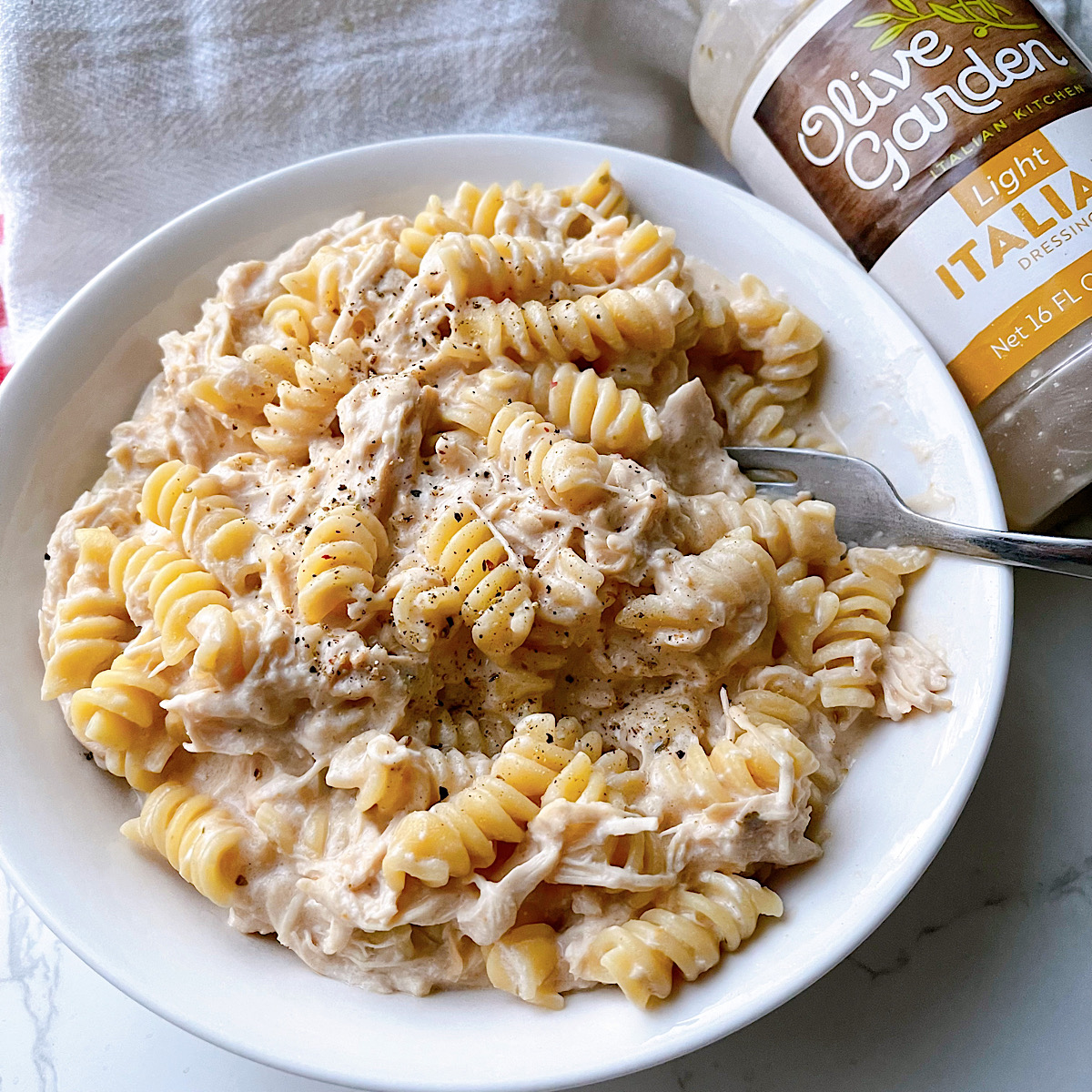 A bowl of chicken pasta and a bottle of Olive Garden Salad Dressing.