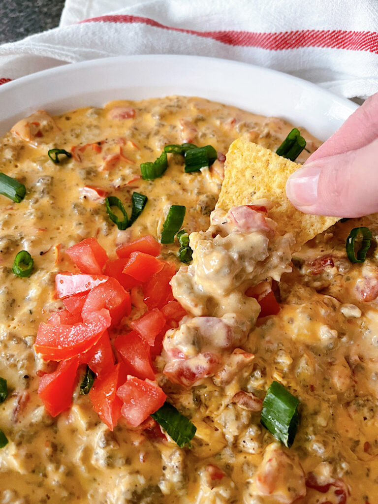 A dish of cheesy Rotel dip with sausage next to tortilla chips.