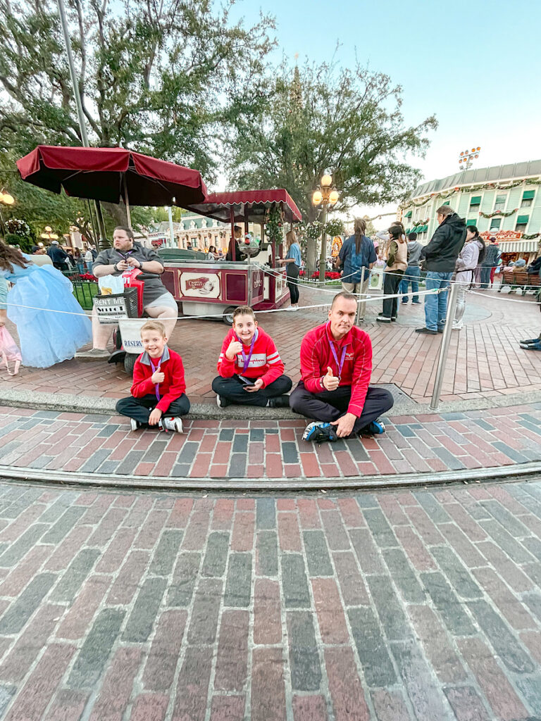 Three people sitting in the reserved area for the Christmas Fantasy Parade at Disneyland.