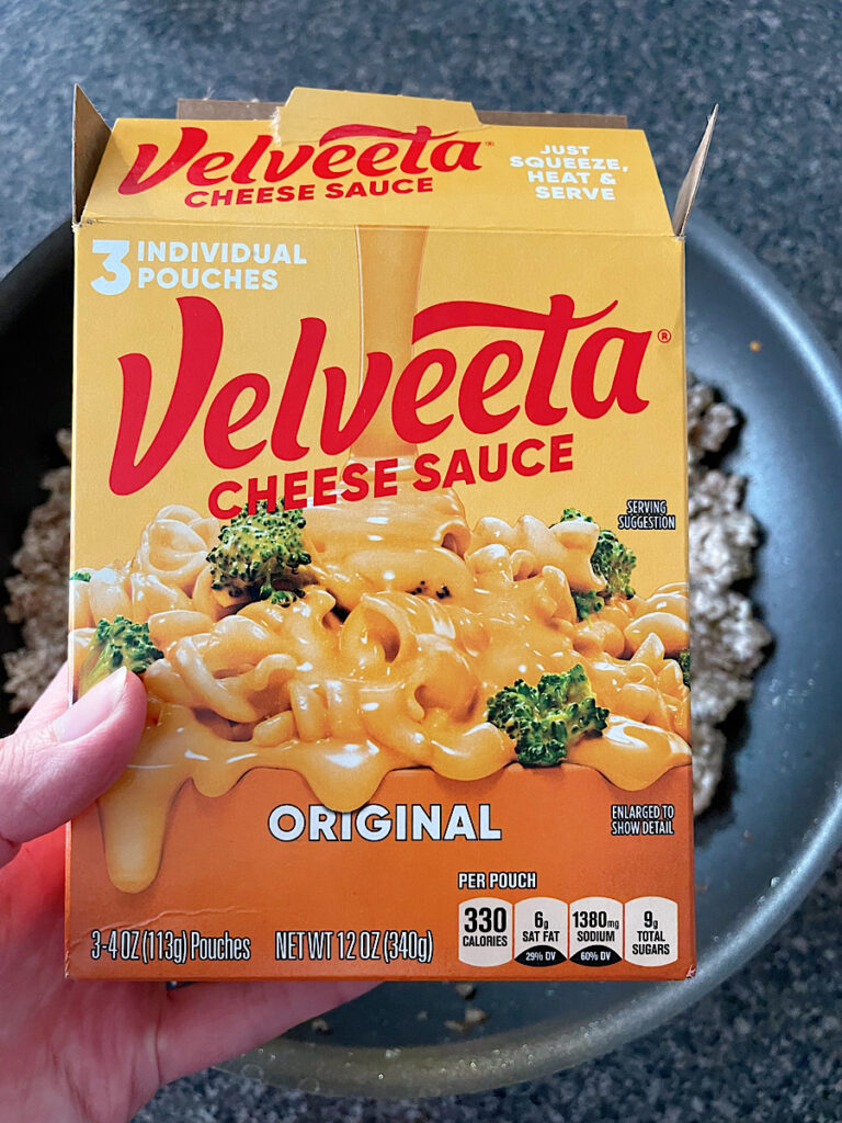 A box of Velveeta cheese sauce over a pan of cooked ground sausage.