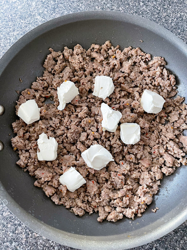 Ground sausage in a pan with cubes of cream cheese.