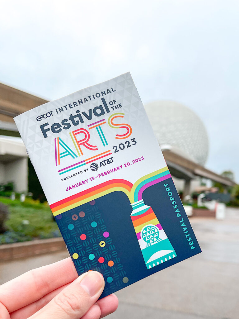 Epcot Festival of the Arts food guide book in front of Spaceship Earth at Epcot.