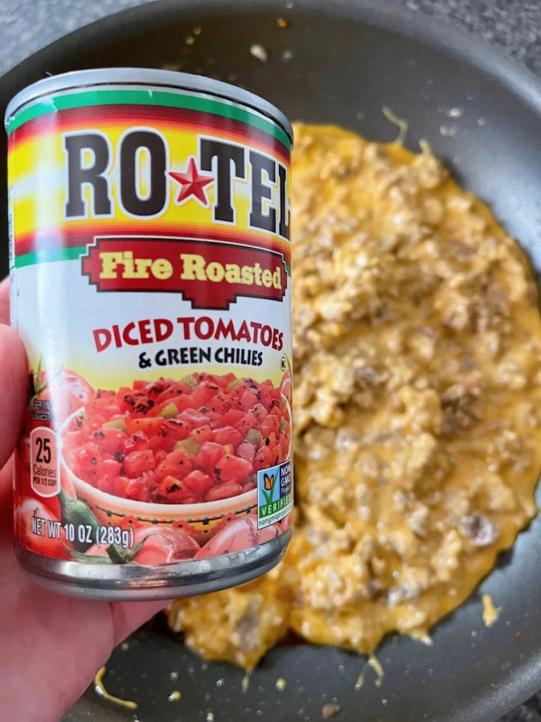 A can of Rotel tomatoes over a pan of melted cheese and sausage.