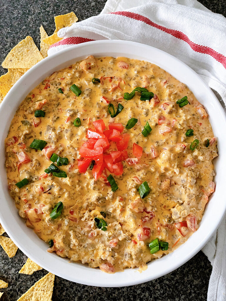 A dish of cheesy Rotel dip with sausage next to tortilla chips.