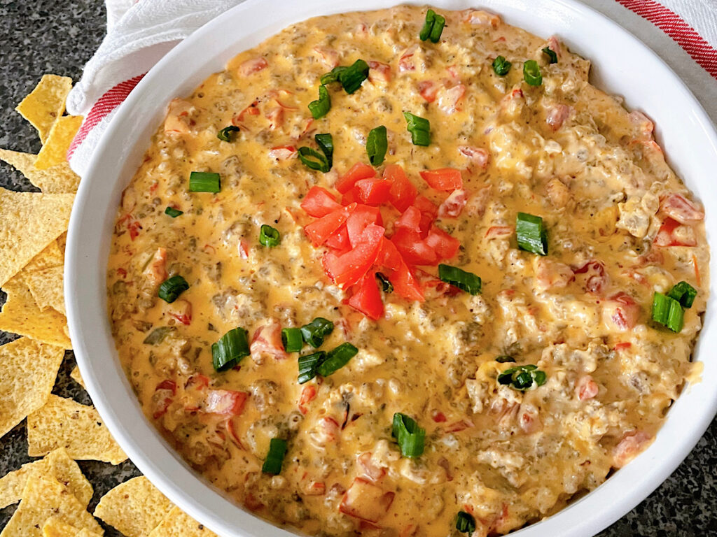 A dish of cheesy Rotel dip with sausage next to tortilla chips.