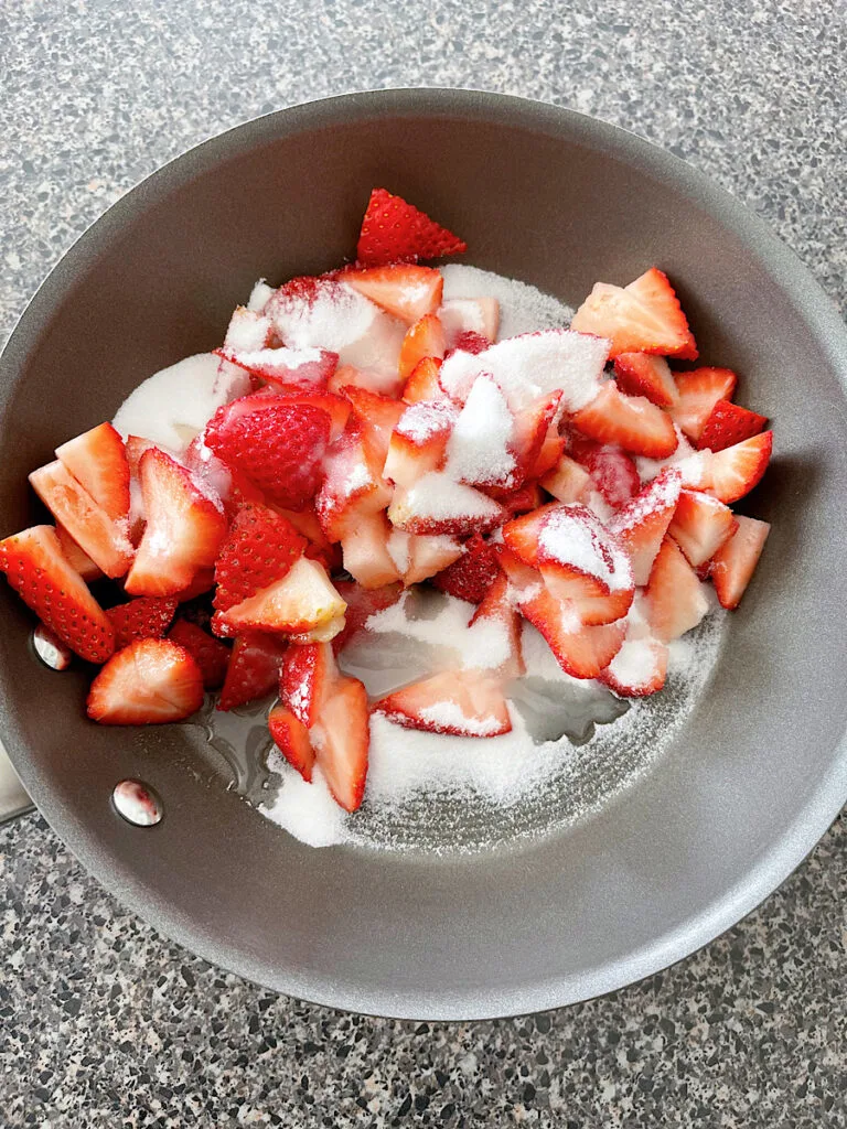 Sliced strawberries with sugar and lemon juice in a sauce pan.
