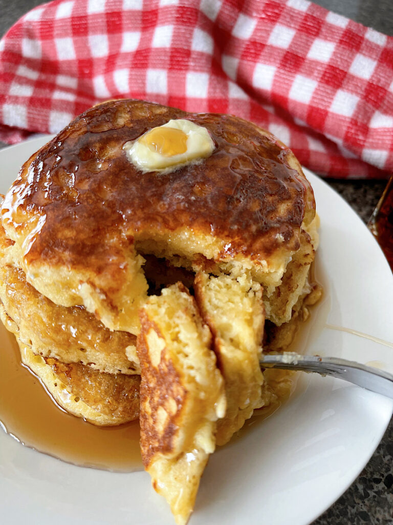 A plate of sour cream pancakes with butter and syrup.