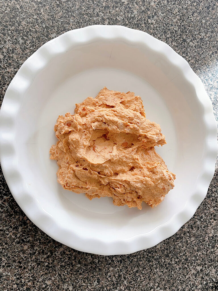 Refried Beans spread into the bottom of a white pie dish.