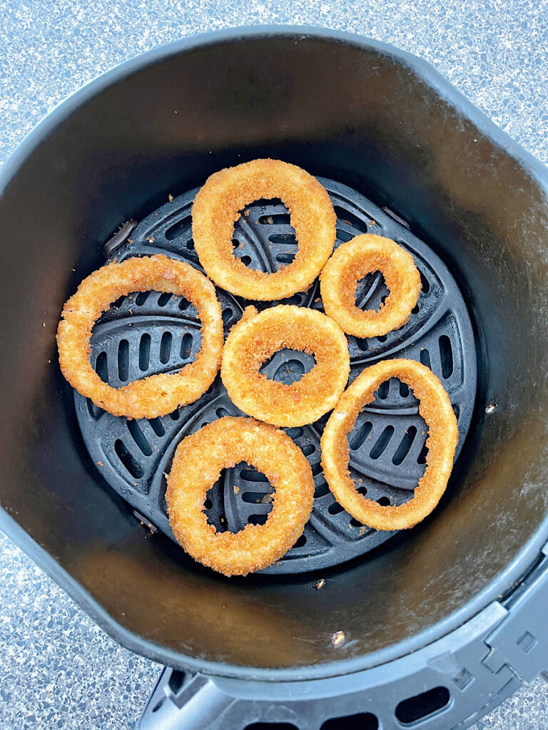 Frozen onion rings in an air fryer basket.