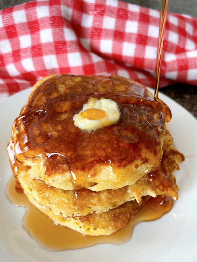 A plate of sour cream pancakes with butter and syrup.