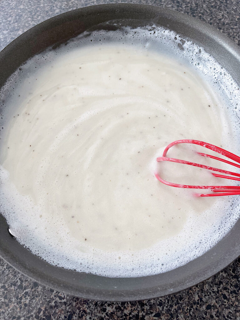 White gravy with a whisk in a pan.