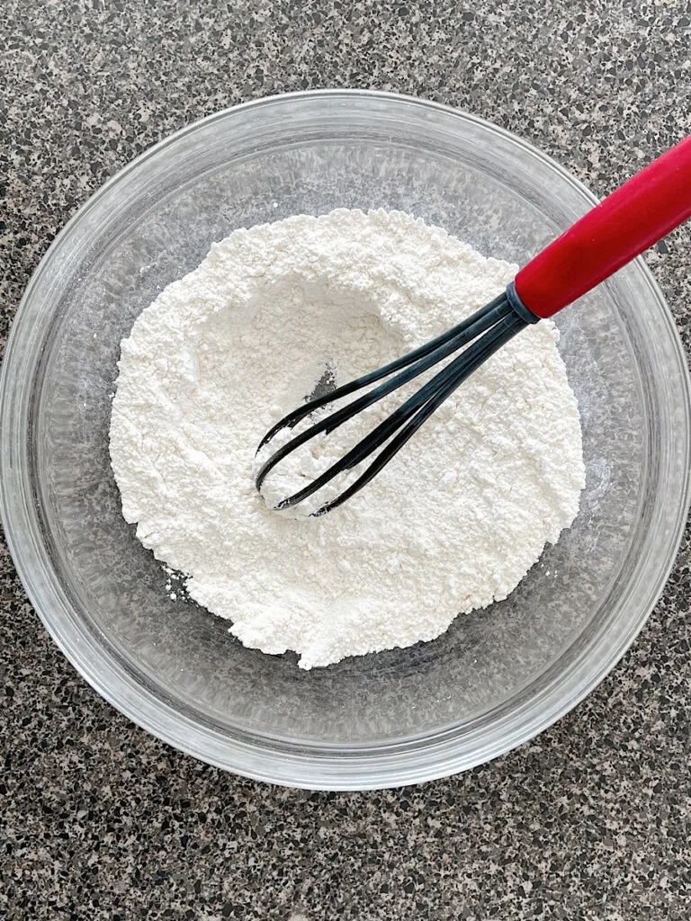 Dry ingredients for sour cream pancakes in a mixing bowl with a whisk.