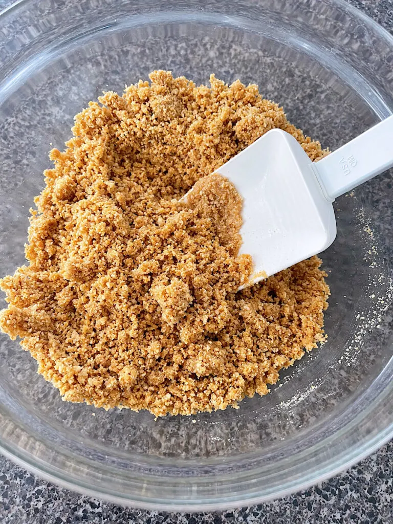 Graham cracker crumbs mixed with melted butter in a bowl.