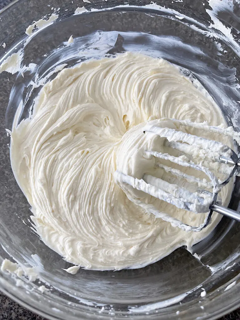 Cream cheese in a bowl with a hand mixer.