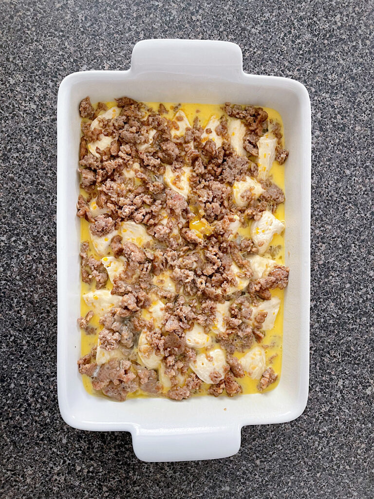 Eggs poured over sausage and biscuits in a baking dish.