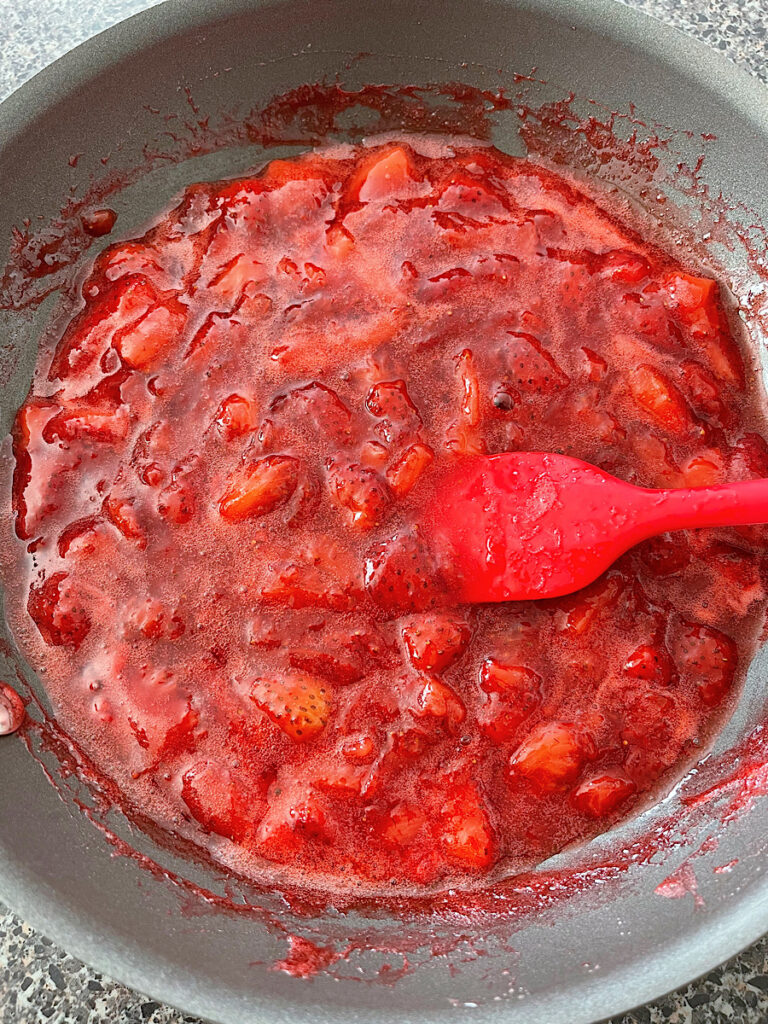 Strawberry sauce in a pan with a red spatula.