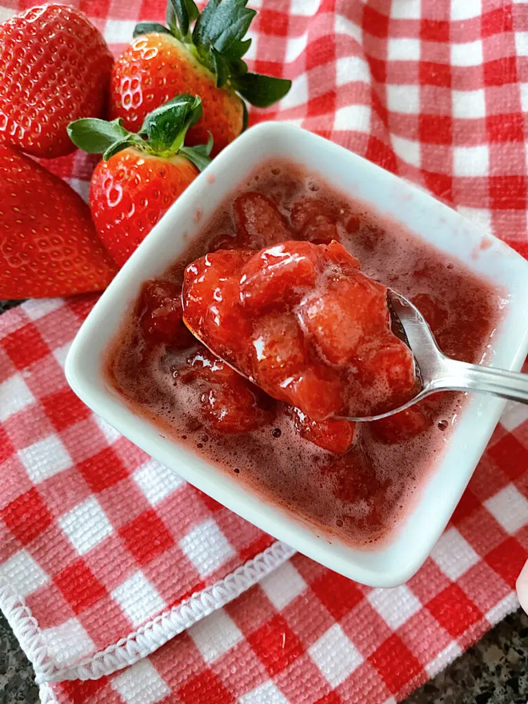A dish of strawberry compote next to fresh strawberries on a red and white towel.