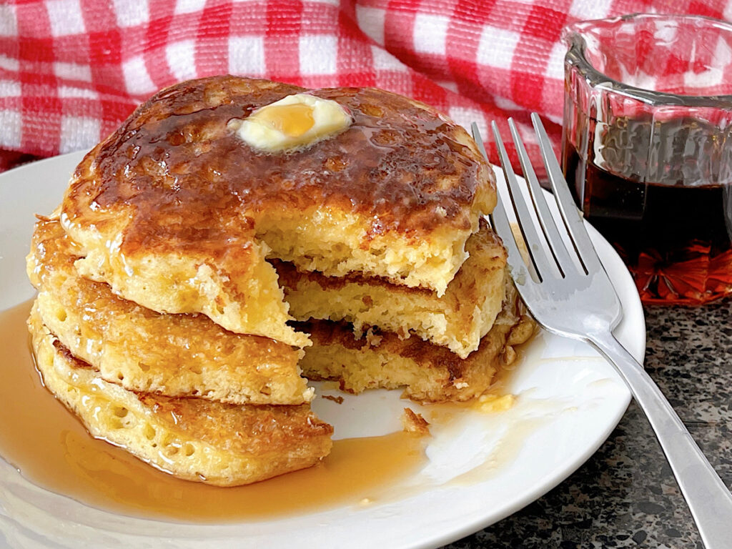 A plate of sour cream pancakes with butter and syrup on a white plate.