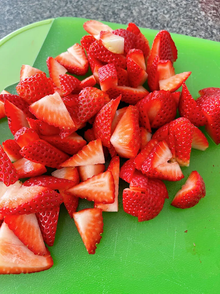 Sliced strawberries on a green cutting board.