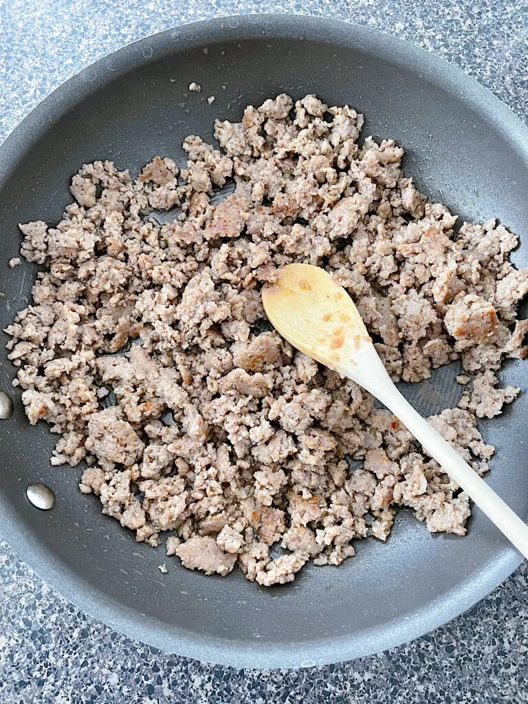 Cooked ground sausage in a frying pan with a wooden spoon.