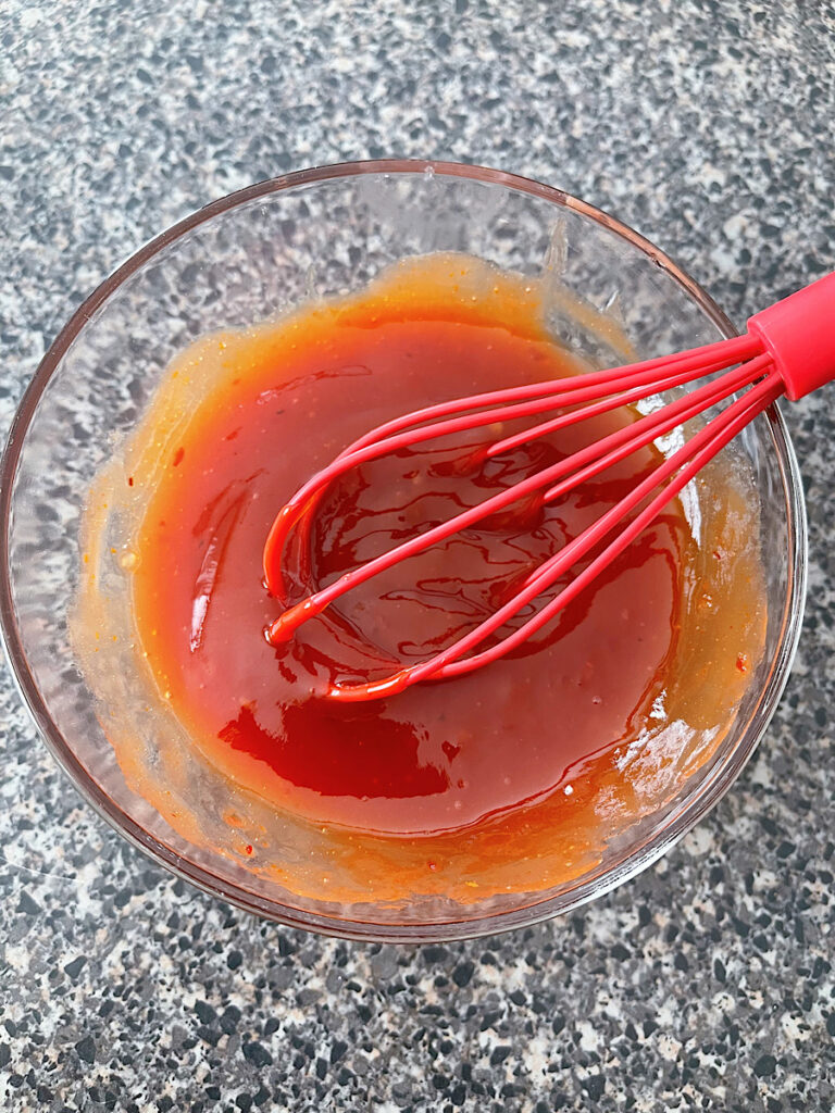 A bowl of spicy ketchup with a red whisk.