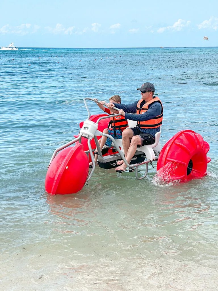 A man and a child on an orange water tricycle in Cozumel beach break excursion.