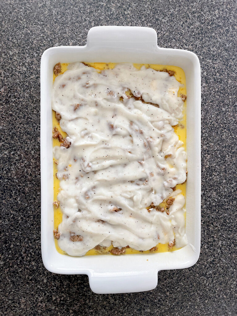 Gravy on biscuits, sausage, and eggs in a baking dish.