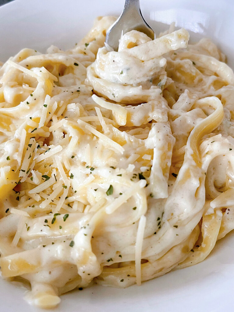 A bowl of Olive Garden Fettuccine Alfredo topped with parmesan cheese and parsley.