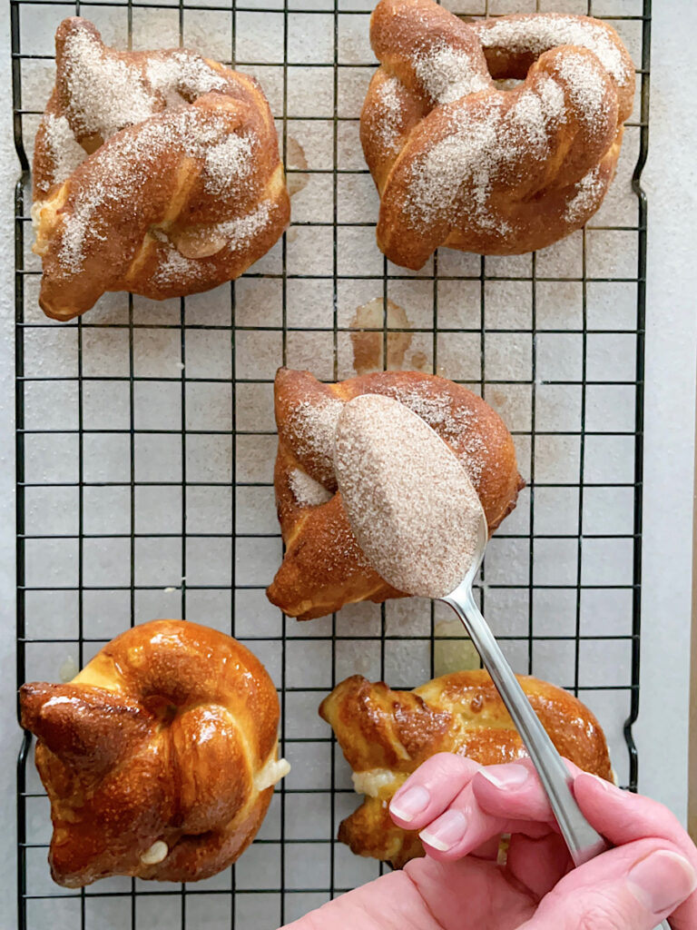 A spoonful of cinnamon sugar held over air fried soft pretzels.