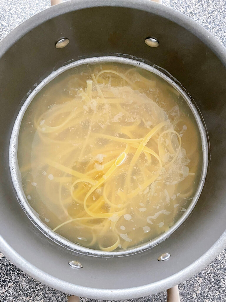 Fettuccine noodles cooking in a pot of water.