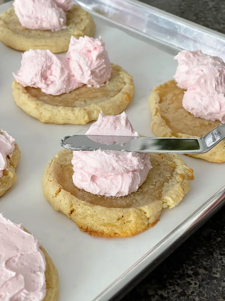 Pink frosting being spread on a sugar cookie with an angled spatula.
