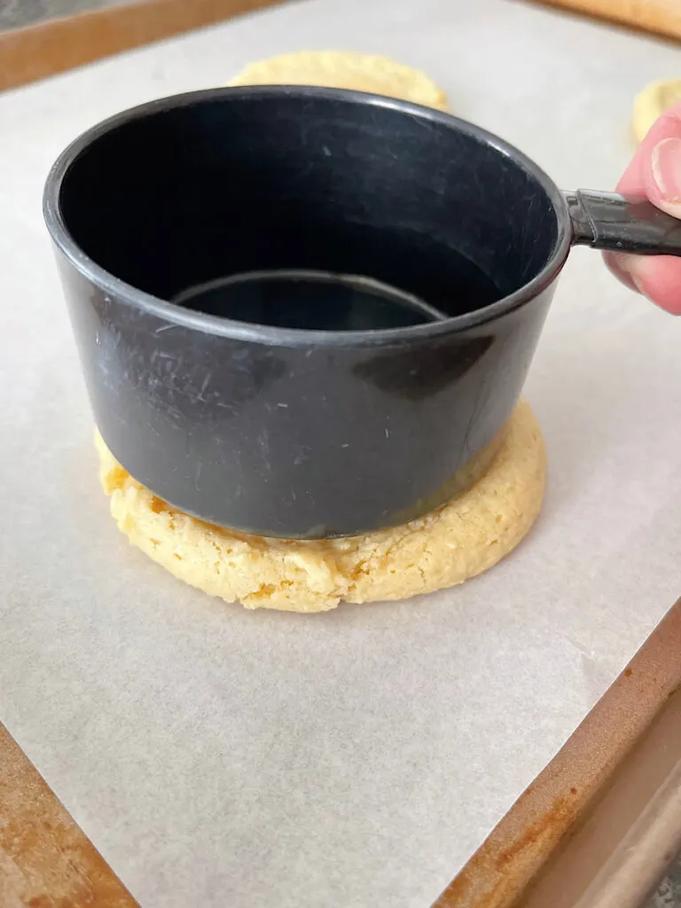 A measuring cup pressed on top of a warm sugar cookie.