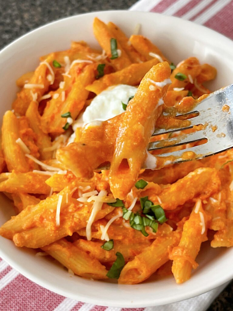 A bowl of homemade Cheesecake Factory Four Cheese Pasta topped with ricotta cheese and chopped fresh basil.