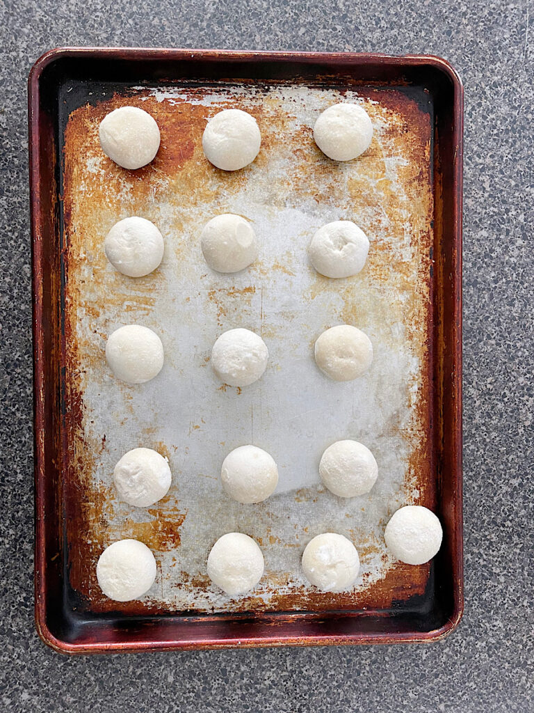 Balls of frozen dough thawing on a baking sheet.