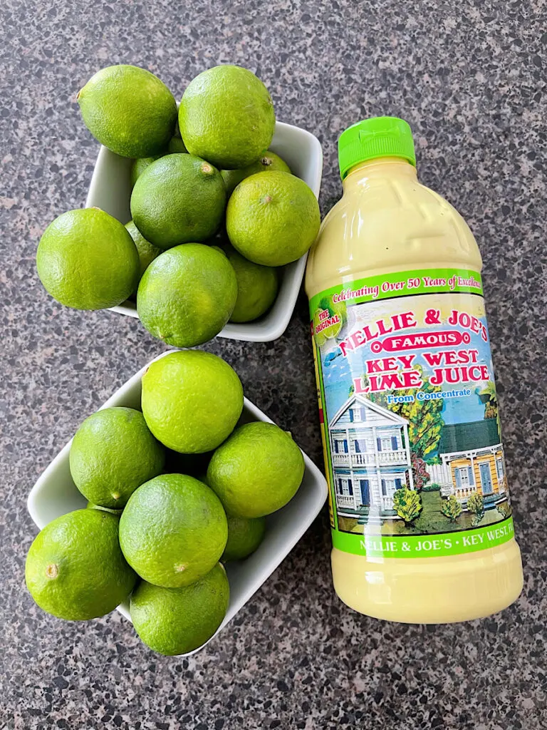 Two bowls of key limes and a bottle of key lime juice.