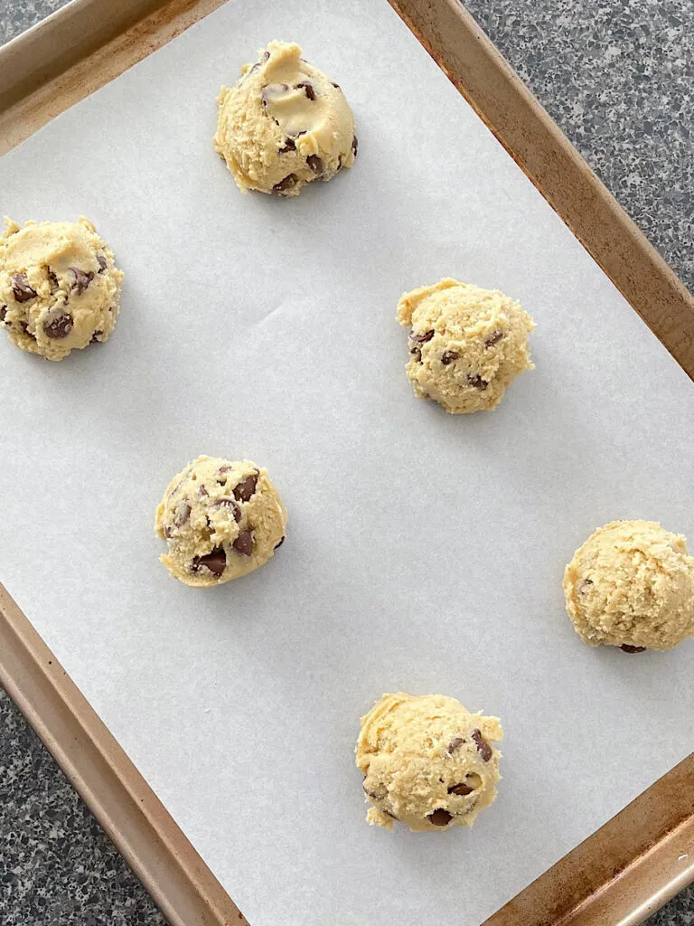 Balls of chocolate chip cookie dough on a baking sheet.