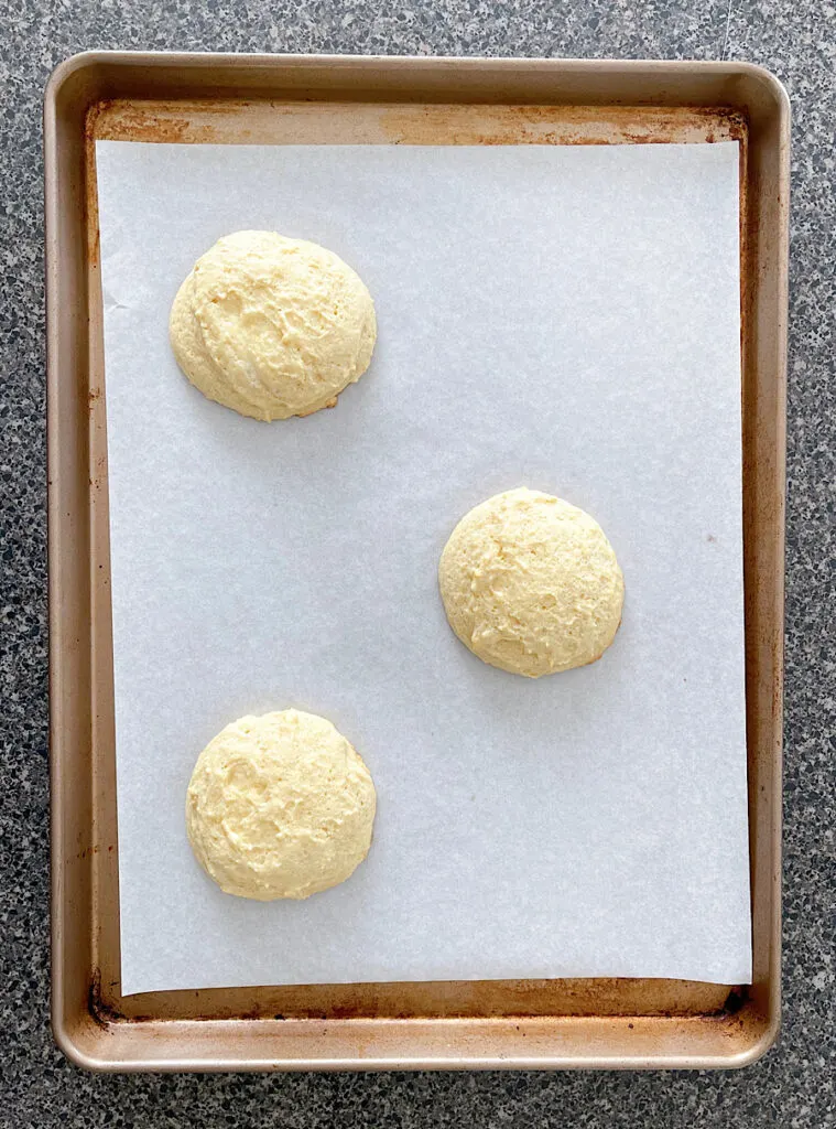 Three large sugar cookies on a baking sheet.