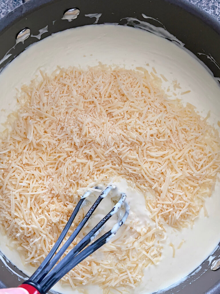 Shredded parmesan added to a saucepan of Olive Garden Alfredo sauce.