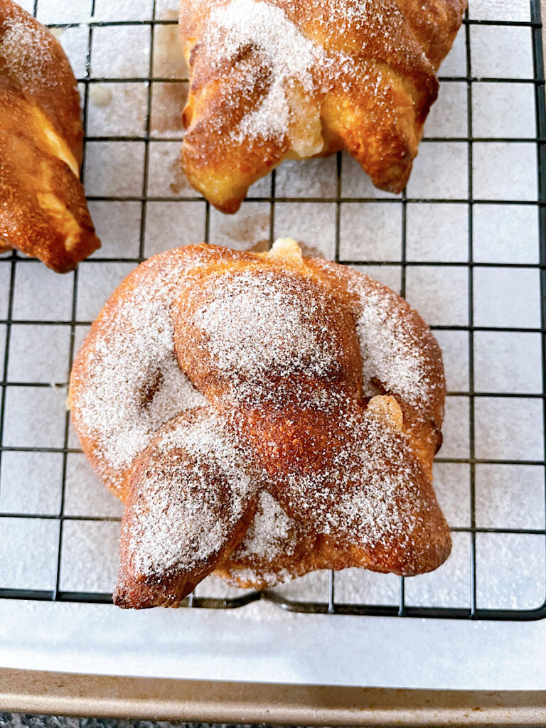 A soft pretzel covered in cinnamon sugar and filled with cream cheese on a wire rack.