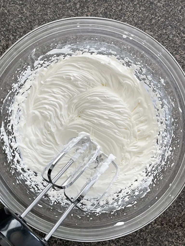 A bowl of whipped cream and an electric hand mixer.