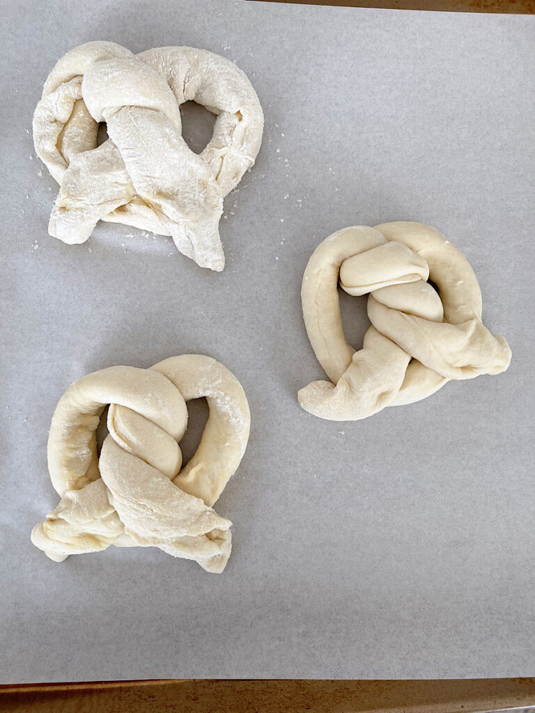 Three uncooked soft pretzels on parchment paper.