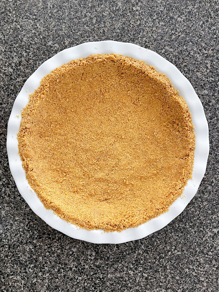 A homemade graham cracker crust in a white pie pan.