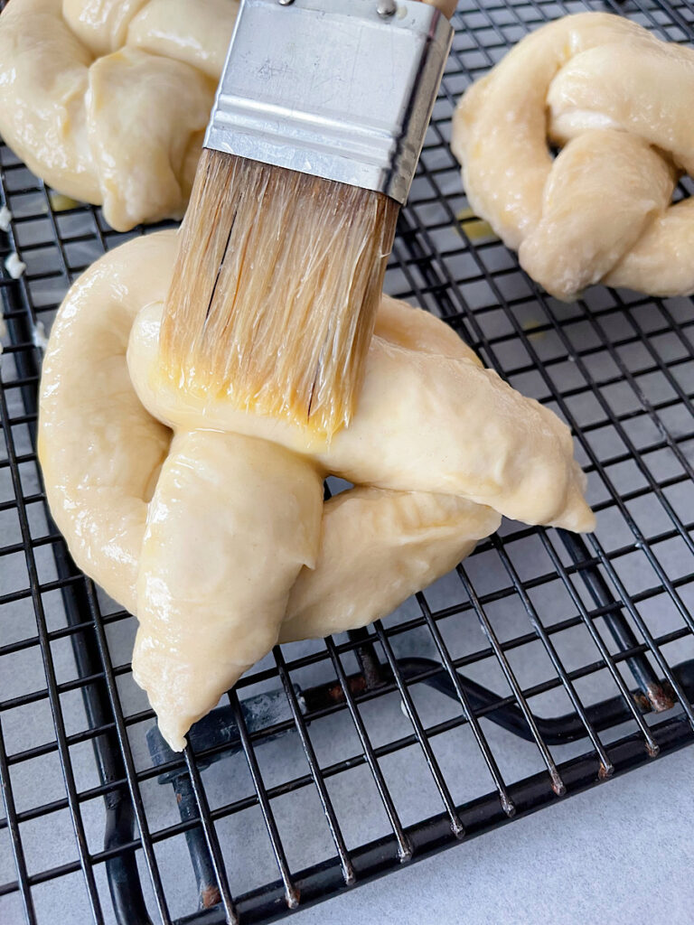 An egg wash being brushed onto a soft pretzel before air frying.