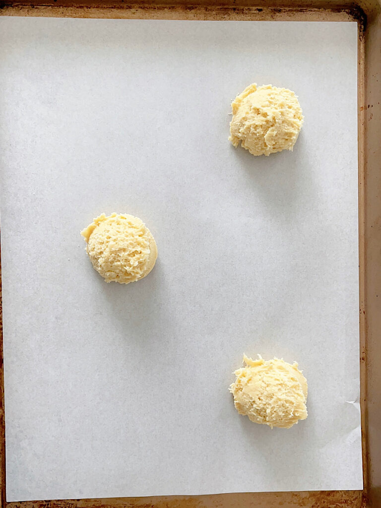 Three balls of cookie dough on a parchment paper lined baking sheet.