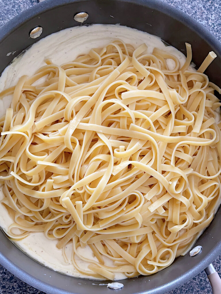 Fettuccine noodles added to a pan of Alfredo sauce.