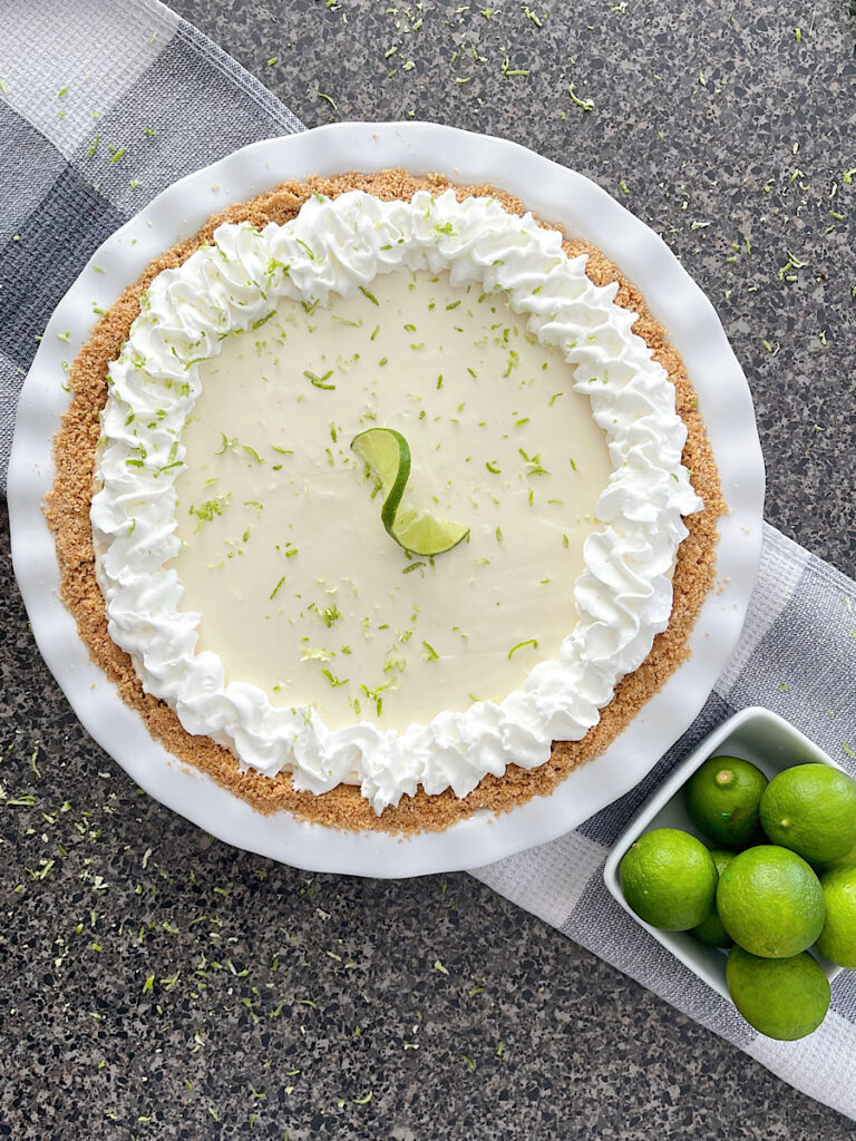 A no bake key lime pie in a white pie plate with a bowl of key limes.